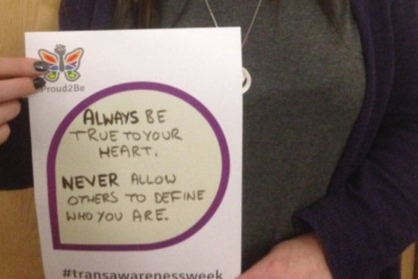 A person holding a hand-written sign reading "Always be true to your heart. Never allow others to define who you are"