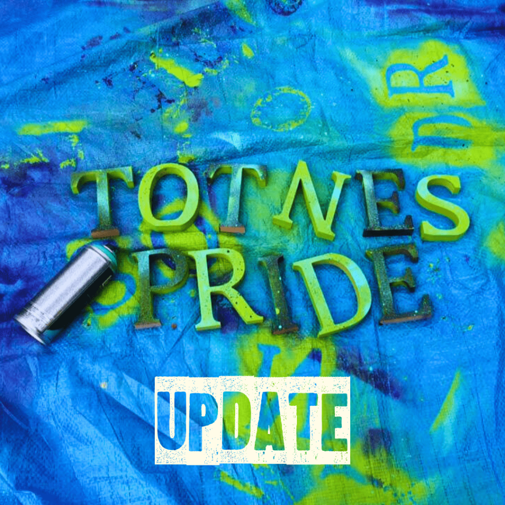 Blue tarpaulin with large cardboard letters spelling out 'Totnes Pride'. On the left of the letters is a spray can laying horizontally. The letters and tarpaulin are randomly sprayed with green and dark blue spray paint. Below is bold transparent text that reads 'update' with a strip of white background.